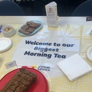 Cancer Council's Welcome to our Biggest Morning Tea sign with cakes, biscuits and napkins