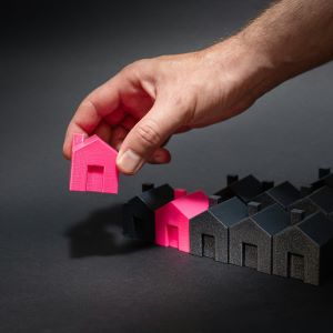 A row of small black and pink houses with a hand picking up a small pink house